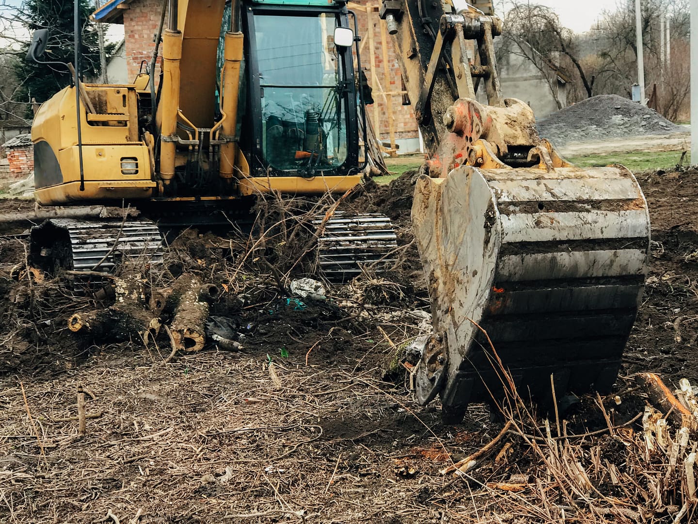 Excavator uprooting trees on rural land in the countryside, clearing space for development.