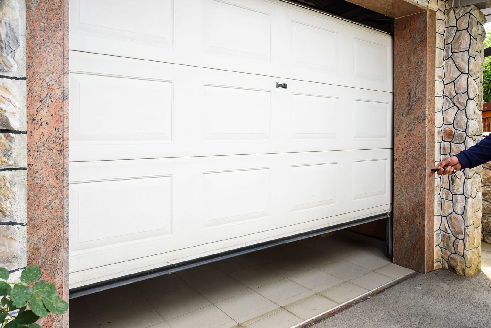 Hand operating a remote controller to open and close a PVC garage door.