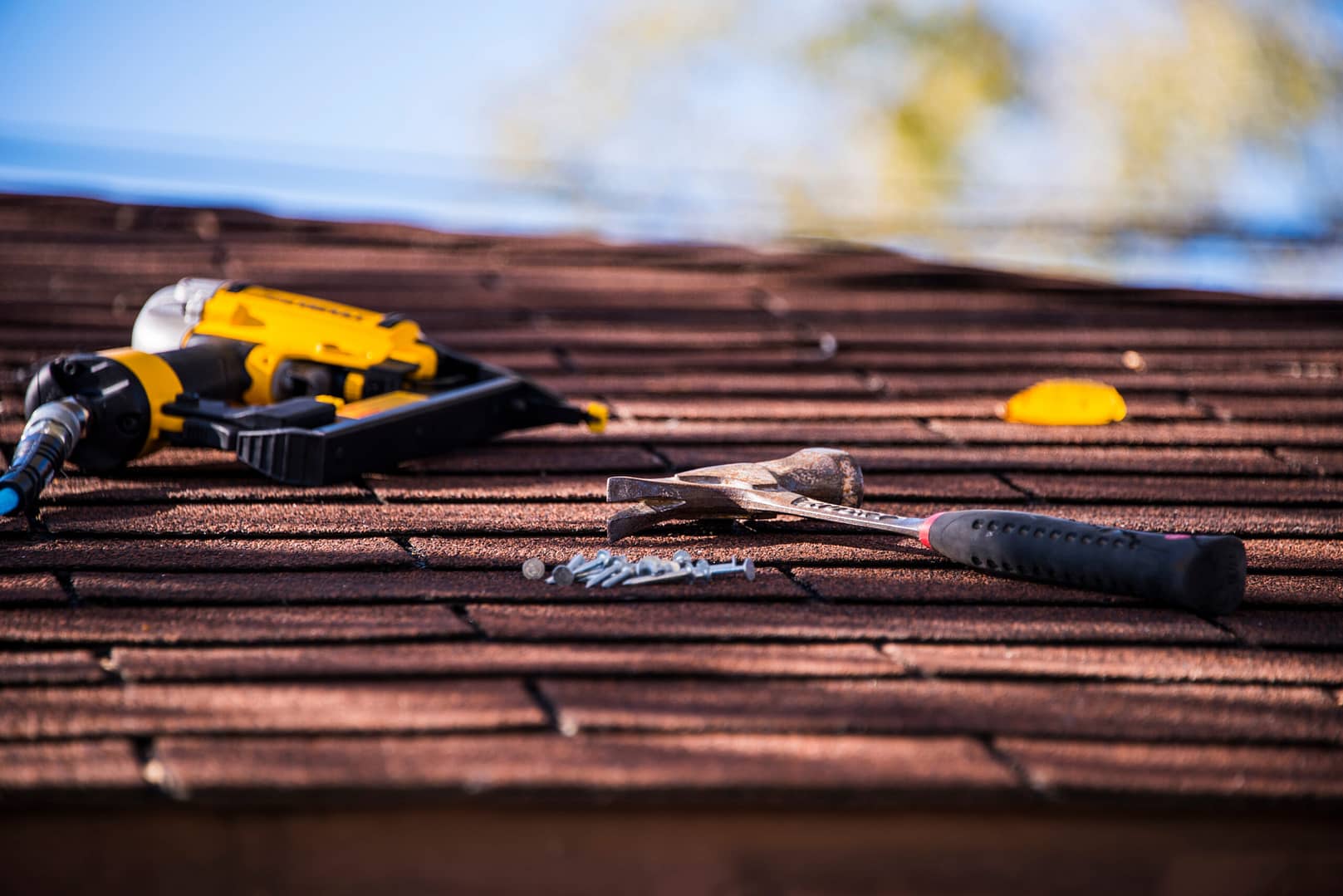 Roof shingle repair in progress, showing a nail gun and hammer being used to secure shingles in place.