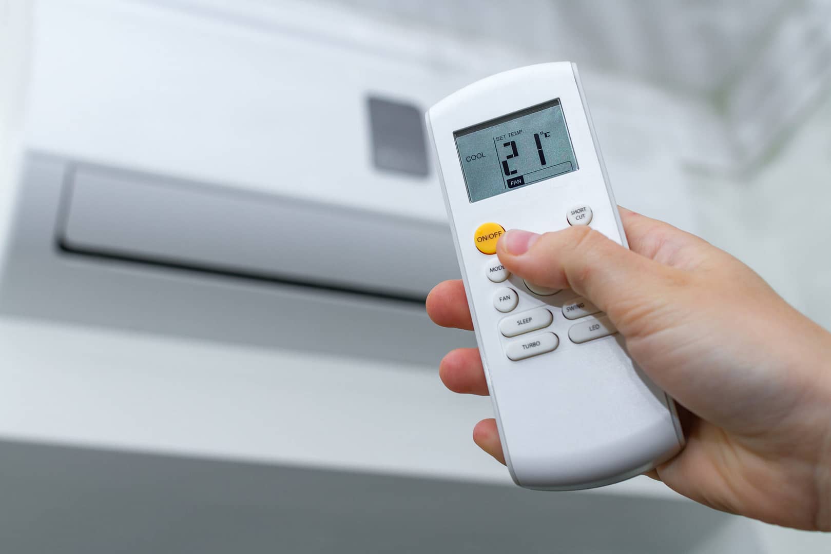 Close up of a hand on a thermostat remote, with an air conditioning unit in the background. Ensure optimal performance and attract more clients with Local Splash's tailored digital marketing strategies