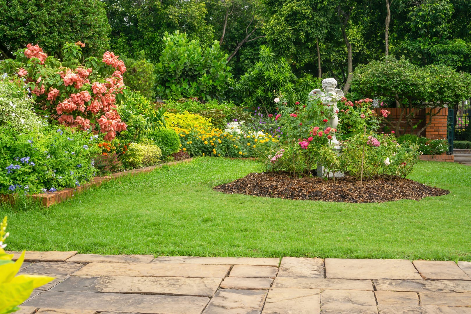 Backyard English cottage garden on brown pavement and green lawn