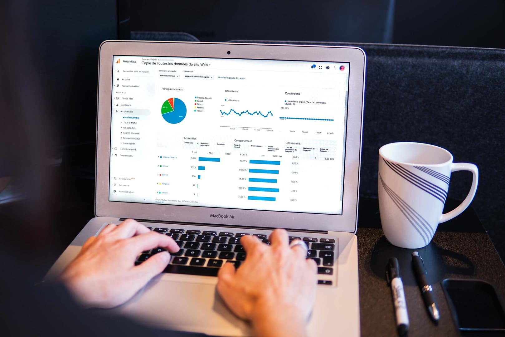 An open laptop displaying marketing statistics on its screen, positioned next to a sleek pen and a coffee mug.