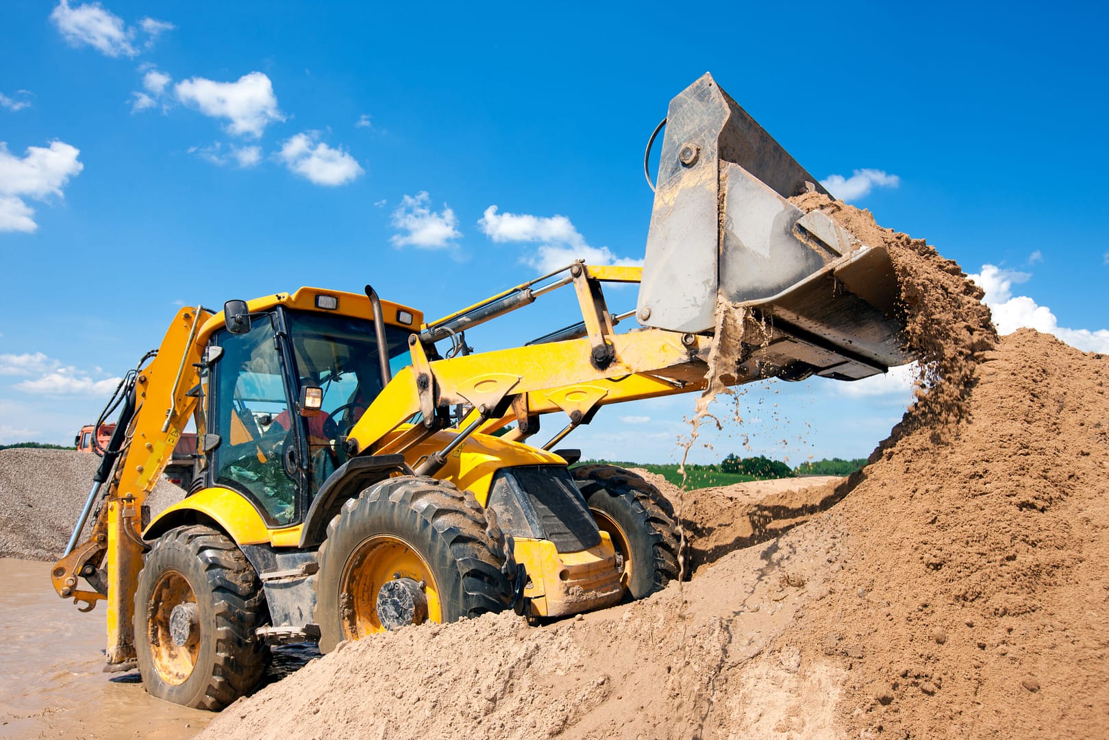 Excavator machine with a bucket unloading sand into a pile at a construction site.