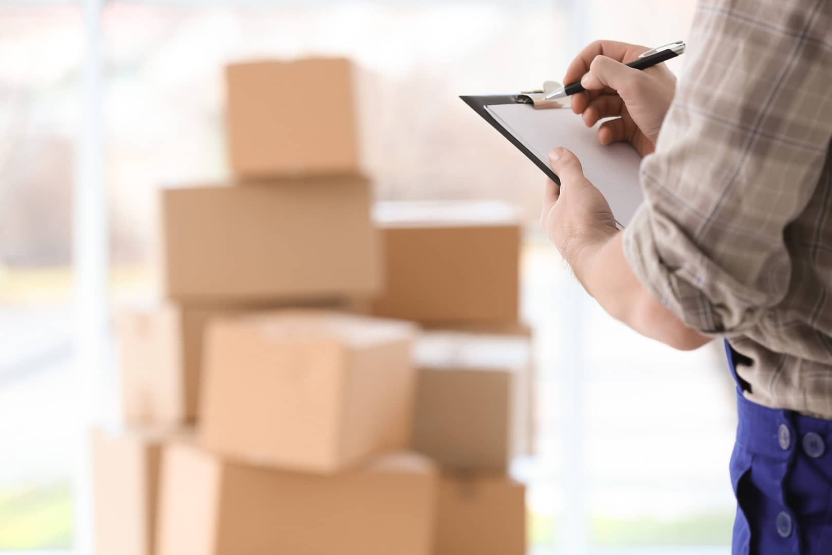 A mover standing with a clipboard in hand against a backdrop of stacked boxes.