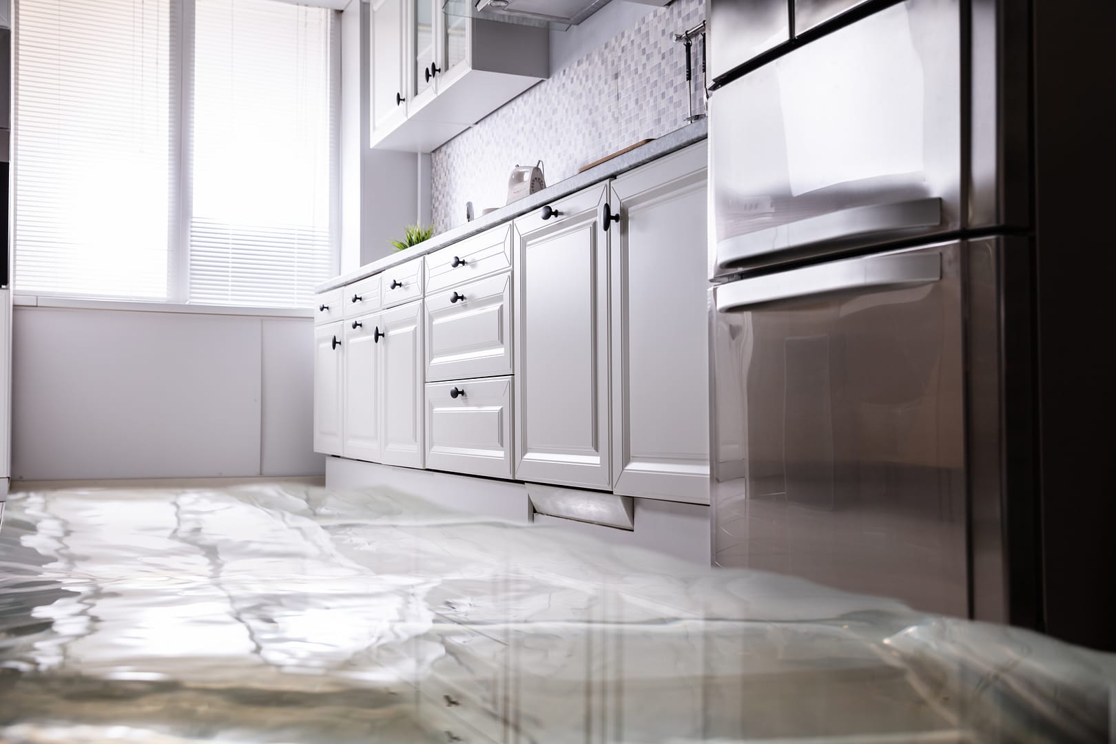 Water puddles on a kitchen floor causing potential damage as it seeps under cabinets.