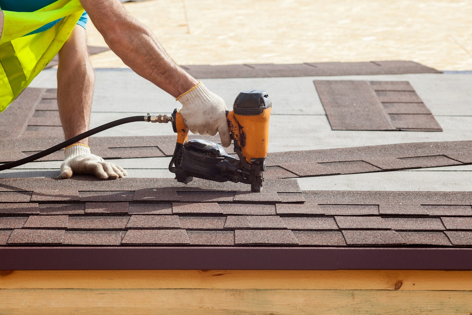 Roofing contractor uses a nail gun to secure asphalt roofing shingles onto the frame of a newly constructed house.