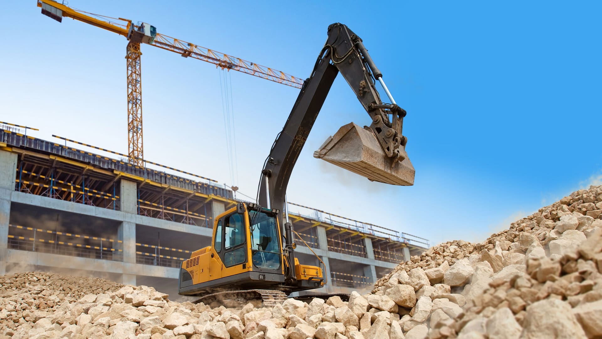 Yellow crawler excavator positioned near an unfinished building, clearing the site in preparation for house construction.