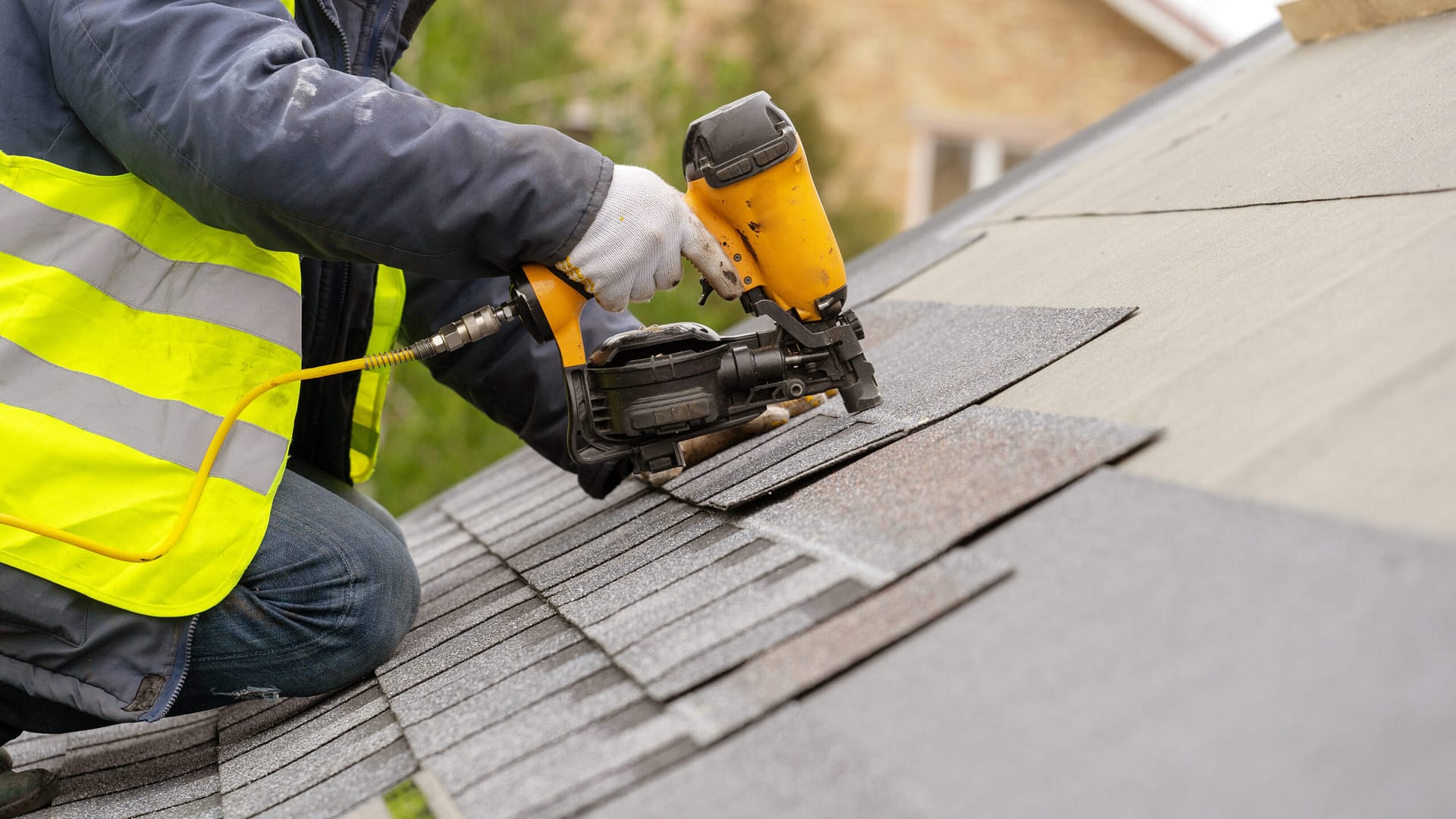 Construction worker using a pneumatic nail gun to install tiles on the roof of a new house.