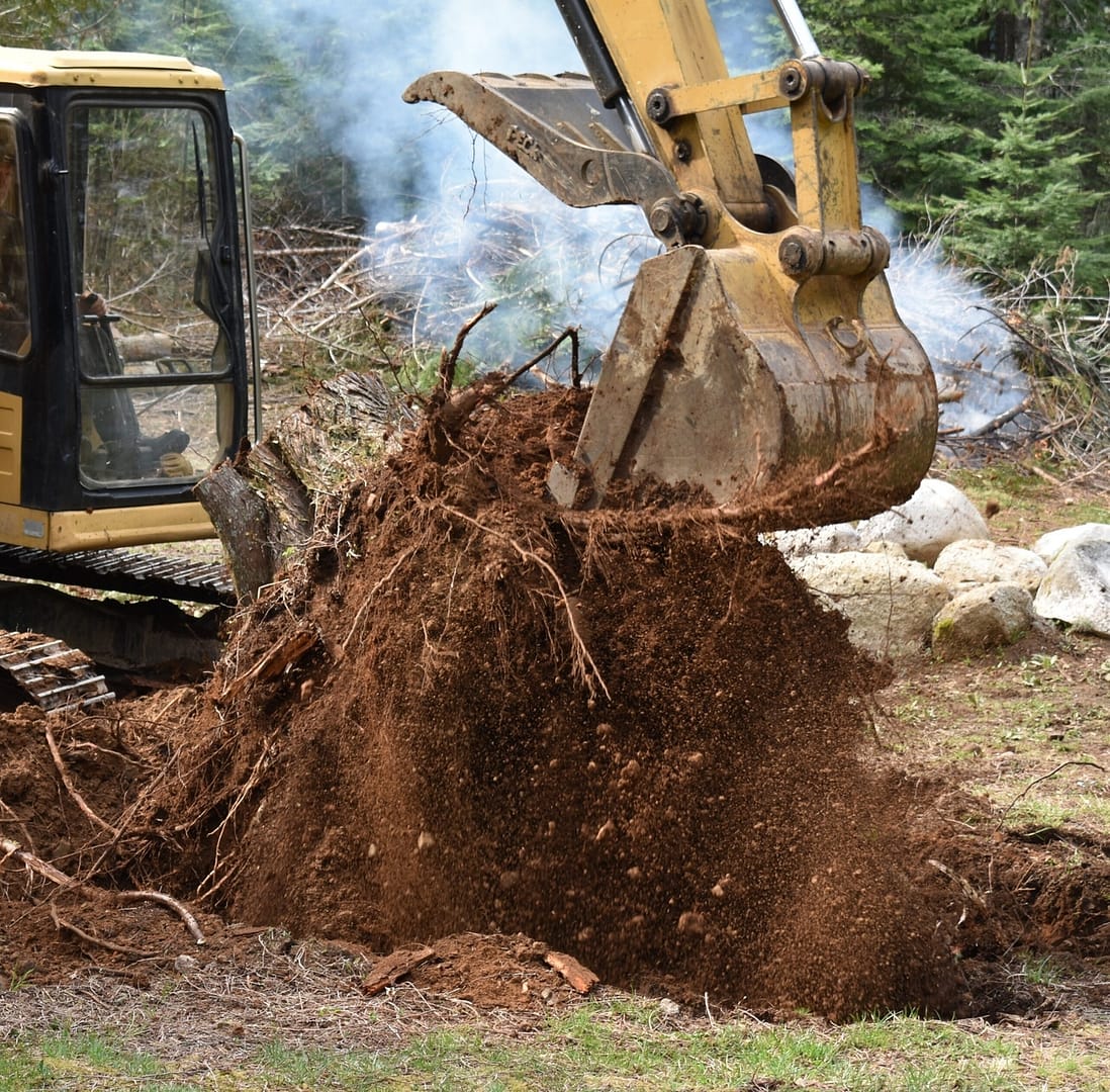 Excavator in action, removing a tree stump from the ground.