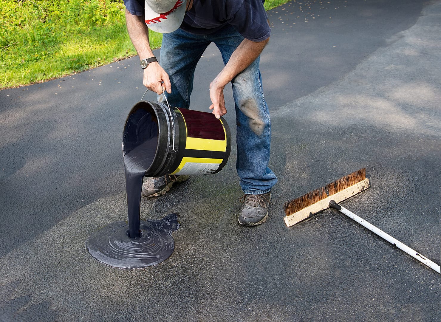 Worker pouring freshly heated asphalt onto a driveway as part of the resealing process.