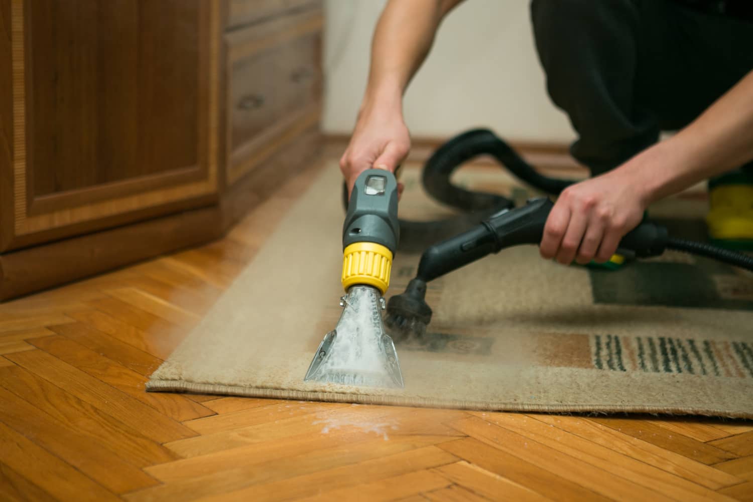 The process of cleaning carpets with a steam vacuum cleaner. An employee of a cleaning company cleans the carpet using steam.