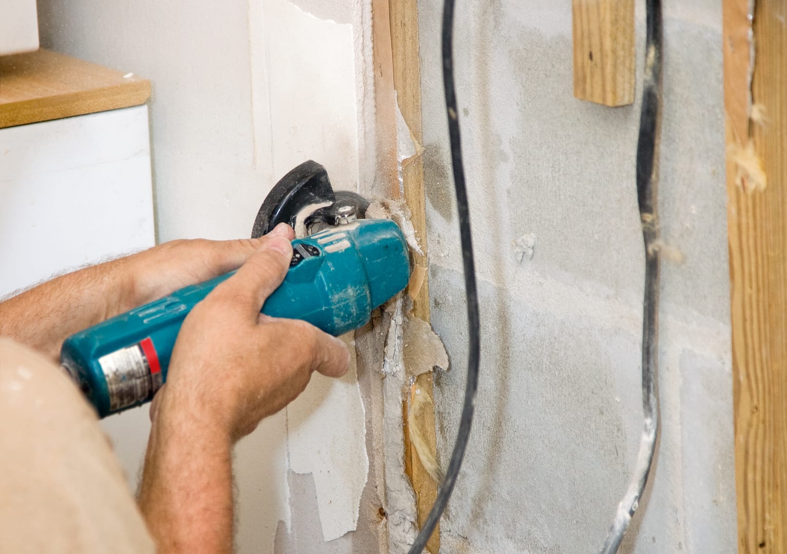 Contractor using an angle grinder to cut through a section of drywall, producing sparks and fine dust as the tool's rotating disc makes contact with the wall material.