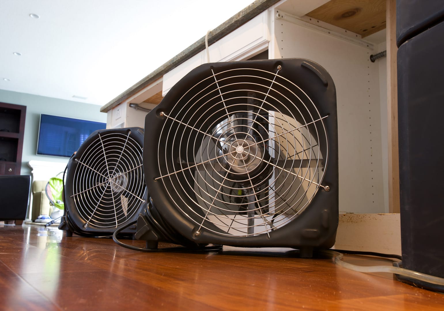 Industrial fans placed in a flooded kitchen, actively drying and ventilating the water-damaged area to prevent mold growth and promote quick recovery.