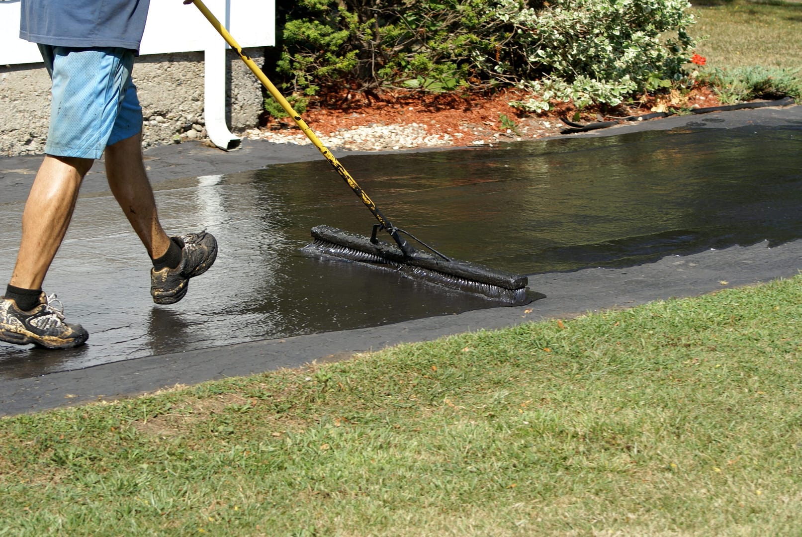Worker carefully applies a thick coat of black driveway sealer to the asphalt surface, ensuring a smooth and protective finish.