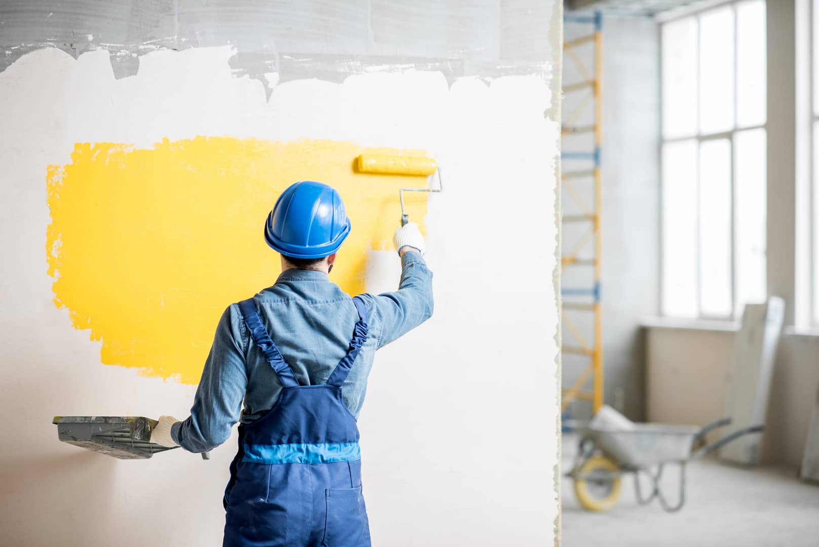 A worker in uniform diligently painting a wall with bright yellow paint.