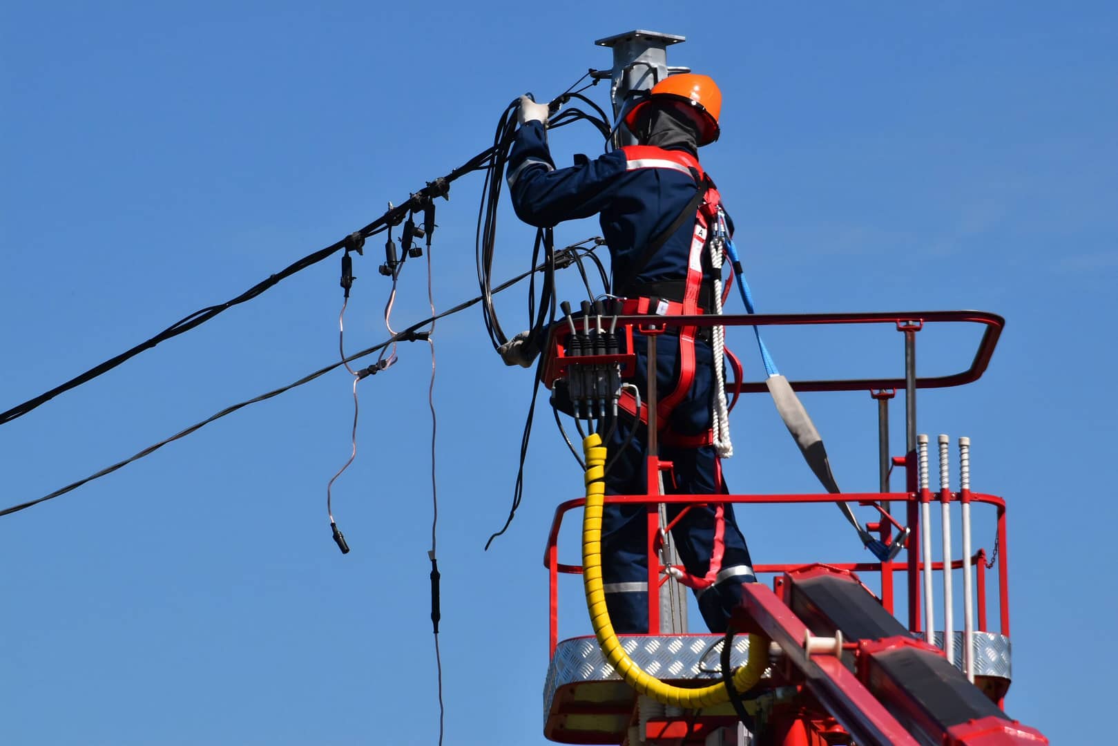 An electrical lineman stands in a basket platform, working on outside power lines wearing a hardhat and safety equipment. It’s important for the electrical contractor you hire to follow all proper safety guidelines, this is why finding a licensed electrician is so important.