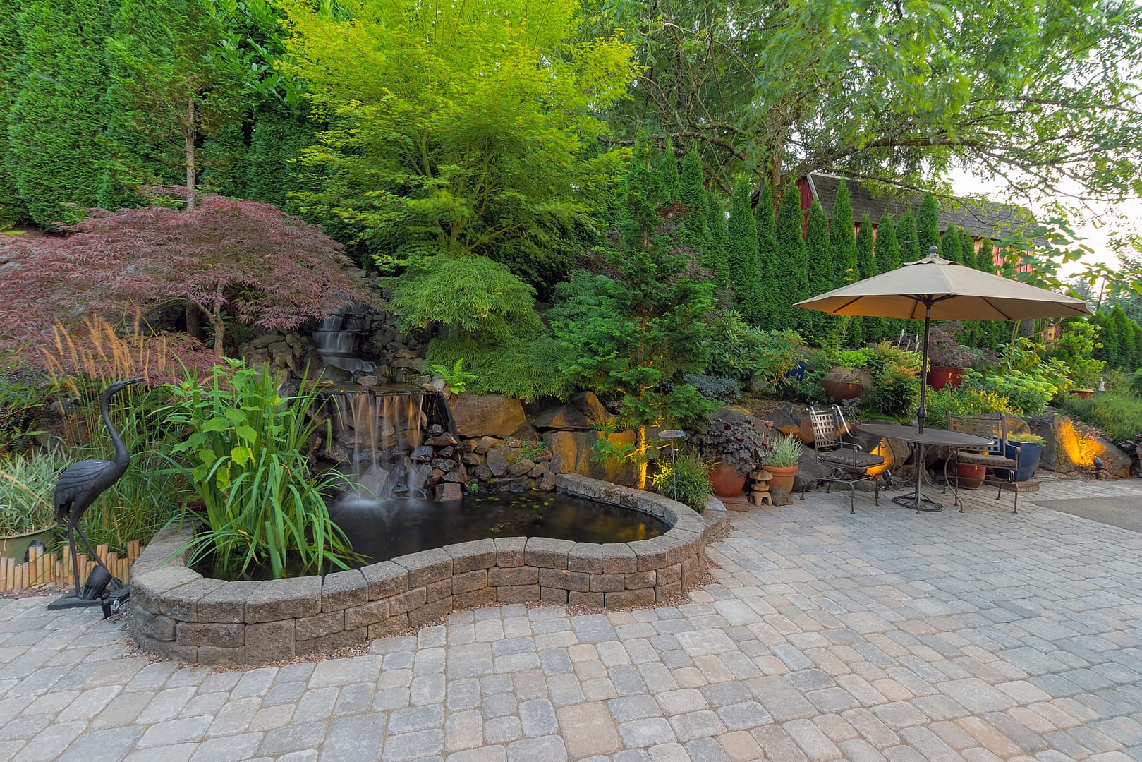 Serene backyard landscaping featuring a spacious patio surrounded by lush greenery and centered around a captivating waterfall pond.