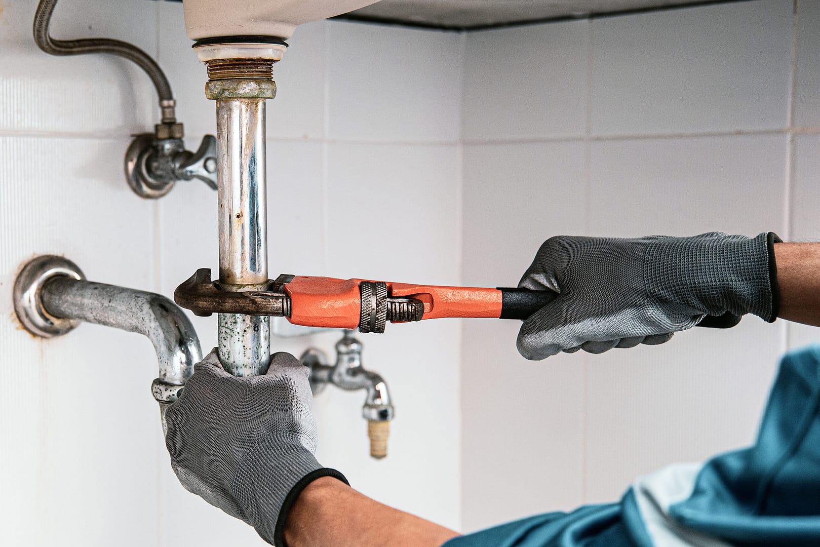 A skilled technician plumber uses a wrench to repair a water pipe under the sink.