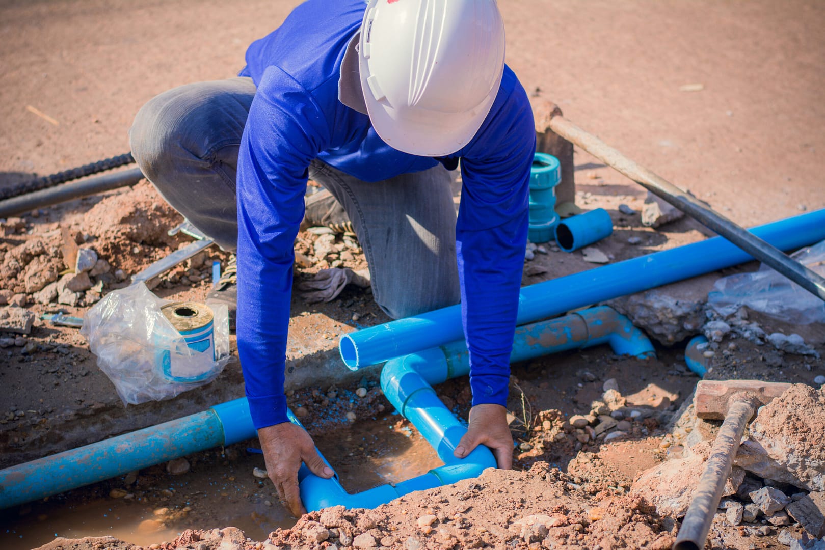 Worker in safety gear repairing a broken water pipe on a concrete road