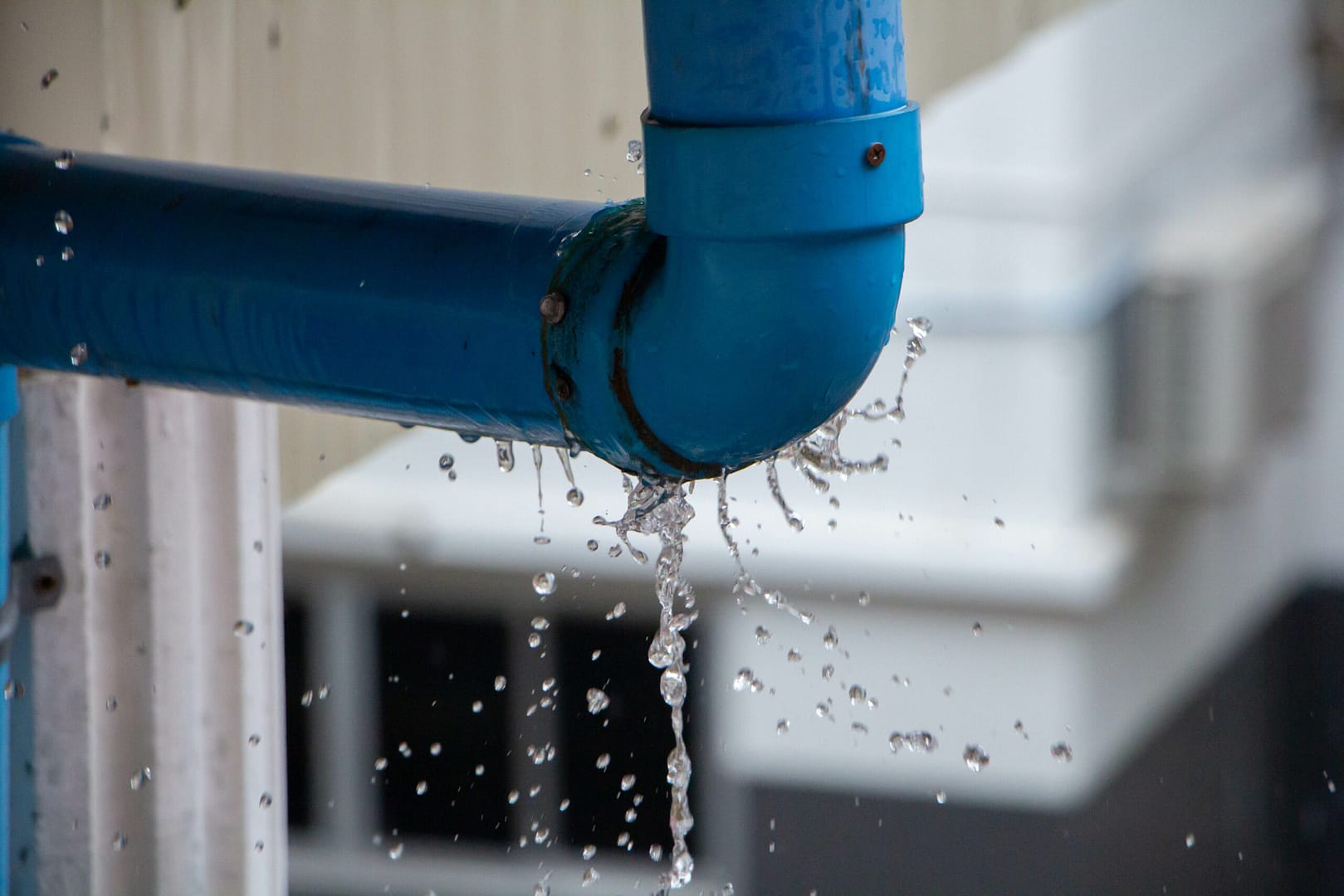 Close-up shot of water leaking and splashing from a plastic pipe, creating dynamic and fluid motion.