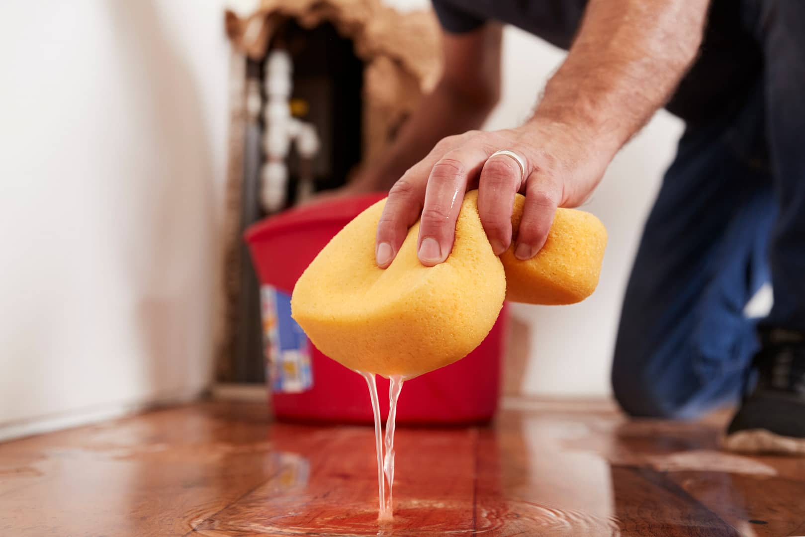 A man diligently cleaning up water from the floor with a sponge, ensuring a dry and safe environment.