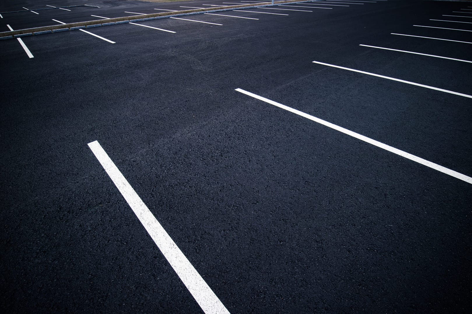 Rows of empty asphalt parking spaces in a well-lit parking lot.