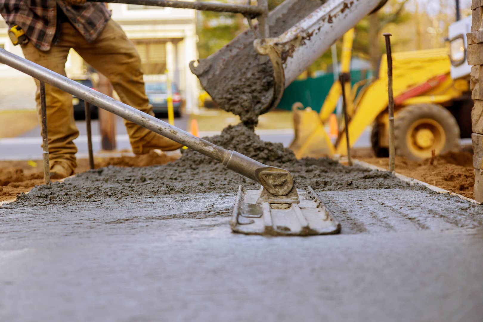 Construction worker pouring and smoothing concrete for ground pavement.