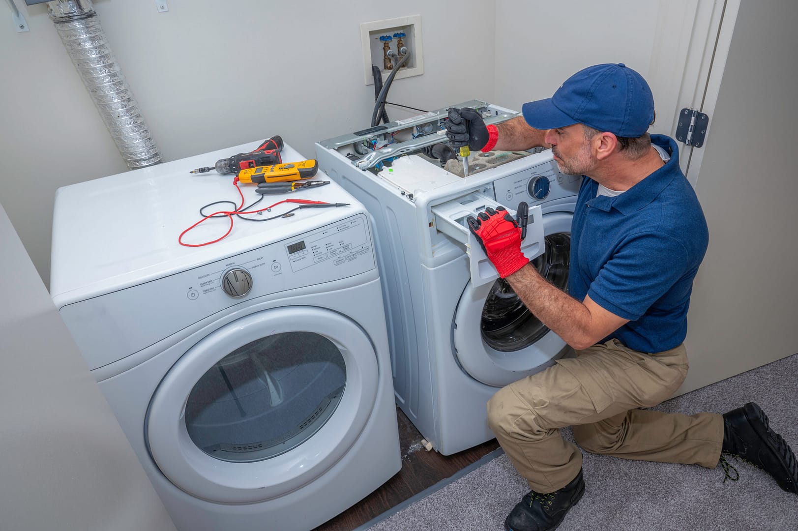 An appliance technician in a laundry room, expertly repairing a front load washing machine.
