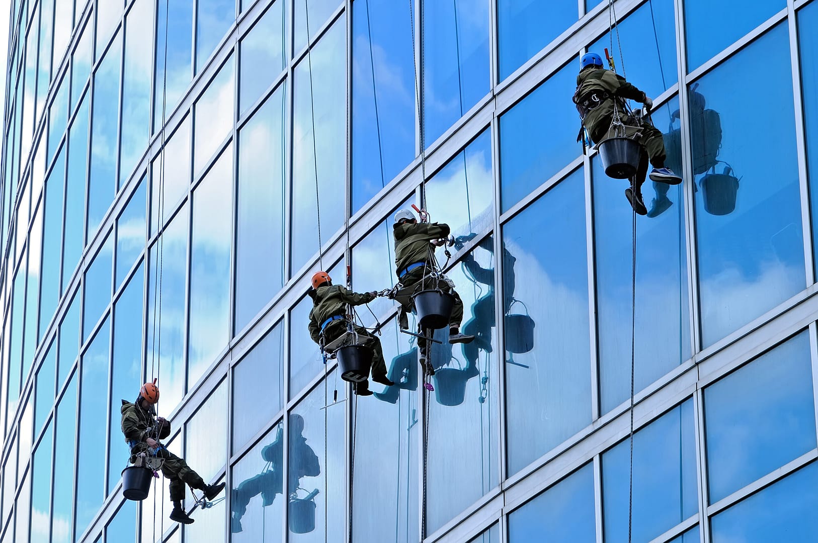 Industrial climbers suspended on ropes washing the windows of a towering skyscraper, high above the city streets.