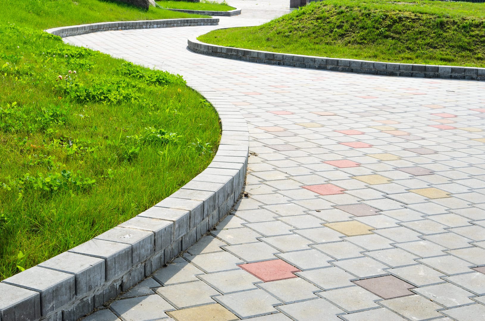 Curved garden path featuring a variety of multicolored sidewalk tiles creating a vibrant and visually appealing walkway through the lush greenery.