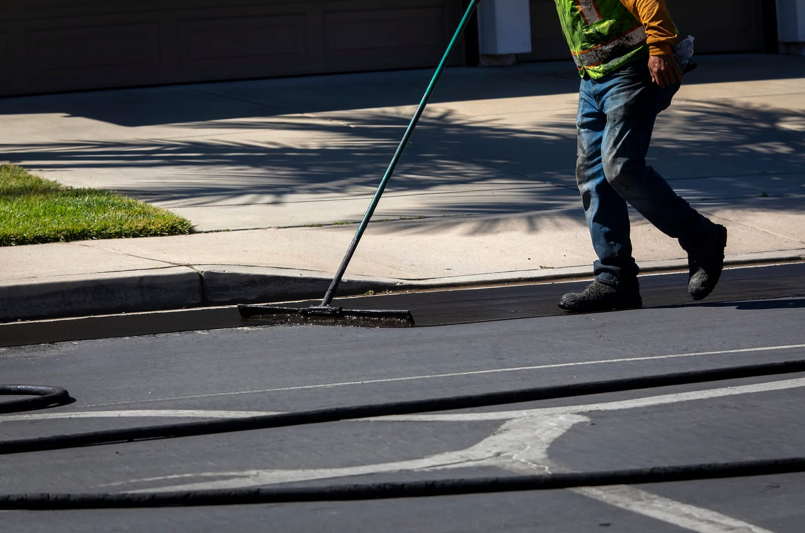 A worker expertly applies sealcoating to asphalt during a resurfacing project using a specialized brush, ensuring a smooth and protective finish.