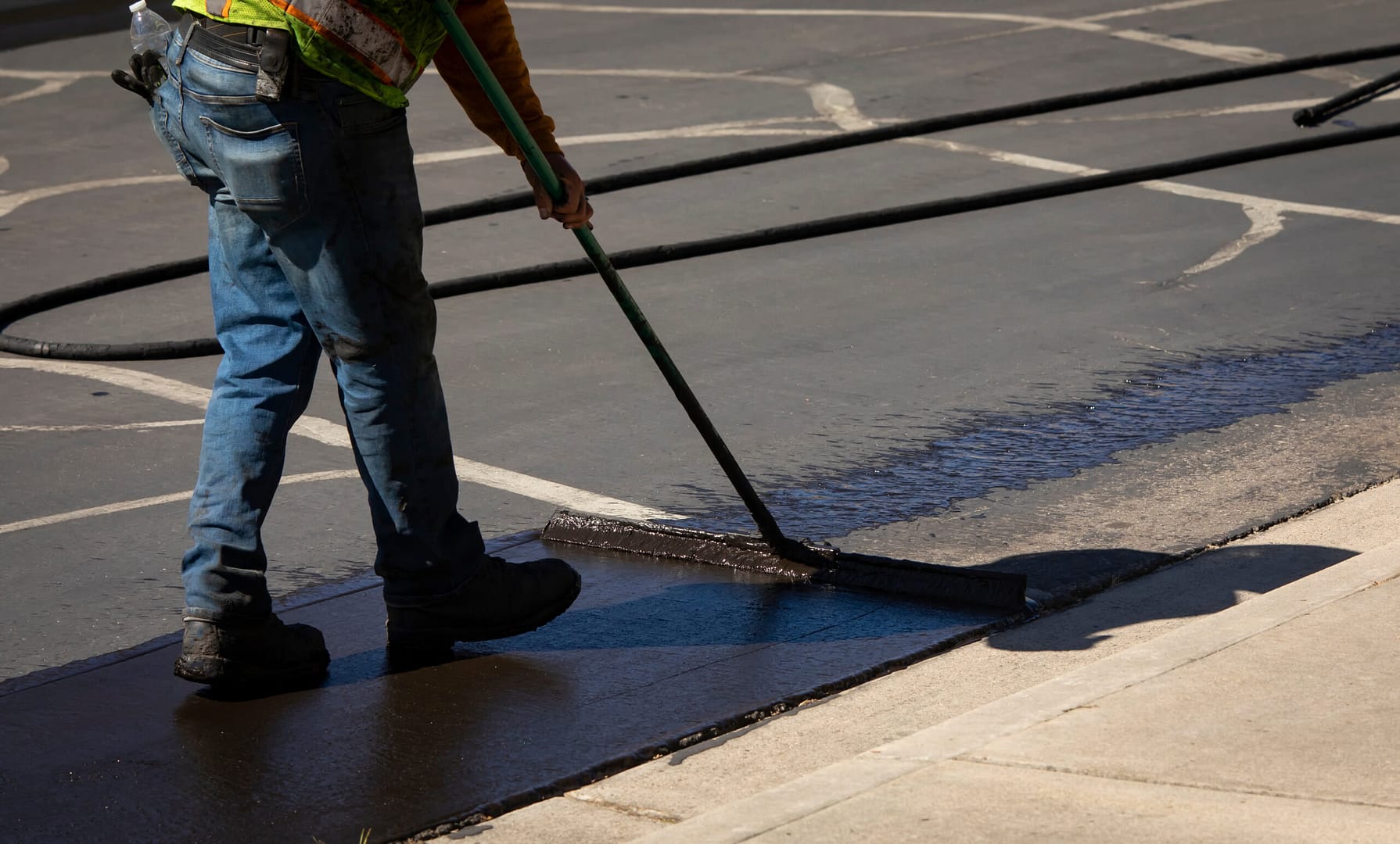 Technician applying slurry sealant on a road, illustrating the advanced maintenance techniques promoted in paving company marketing.
